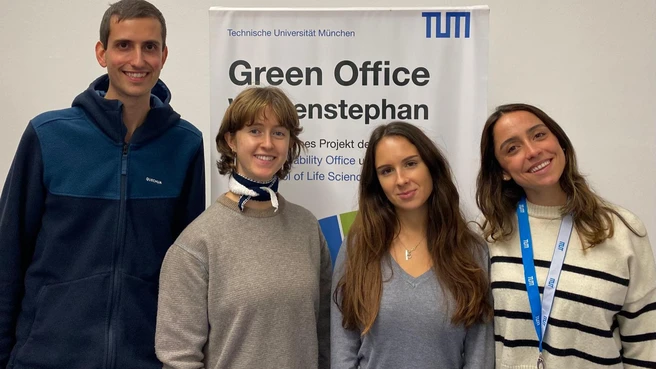 Four Green Office members smiling with banner in background.
